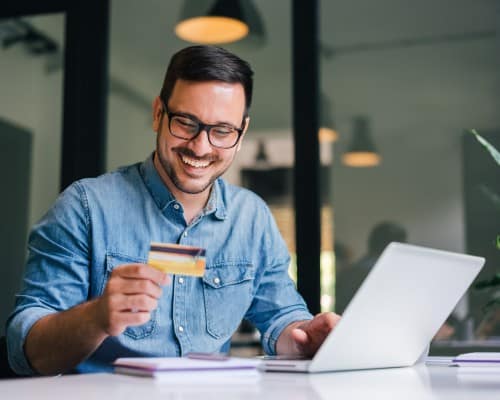 Happy cheerful smiling young adult man making an online payment from his credit card